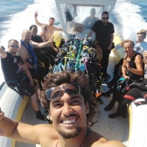 Team istruttori e gruppo subacquei sorridenti su un gommone del Baratti Diving, pronti per un'immersione allo Scoglietto dell'Isola d'Elba