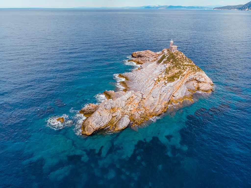 Vista aerea dello Scoglietto all'Isola d'Elba, un isolotto roccioso con faro circondato da acque cristalline turchesi e blu profondo