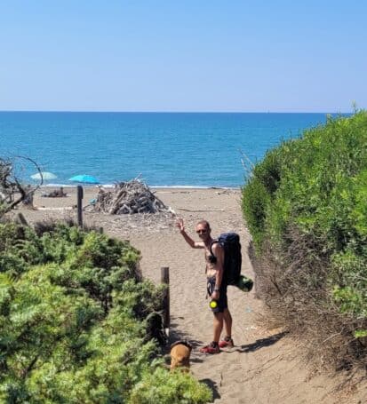 Escursionista con zaino su un sentiero costiero tra la vegetazione mediterranea sulla Costa degli Etruschi