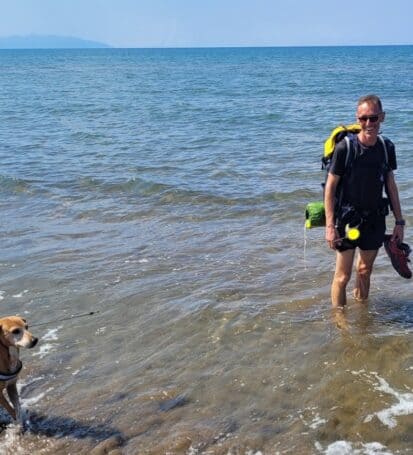 scursionista con zaino e cane che cammina sulla spiaggia della Costa degli Etruschi