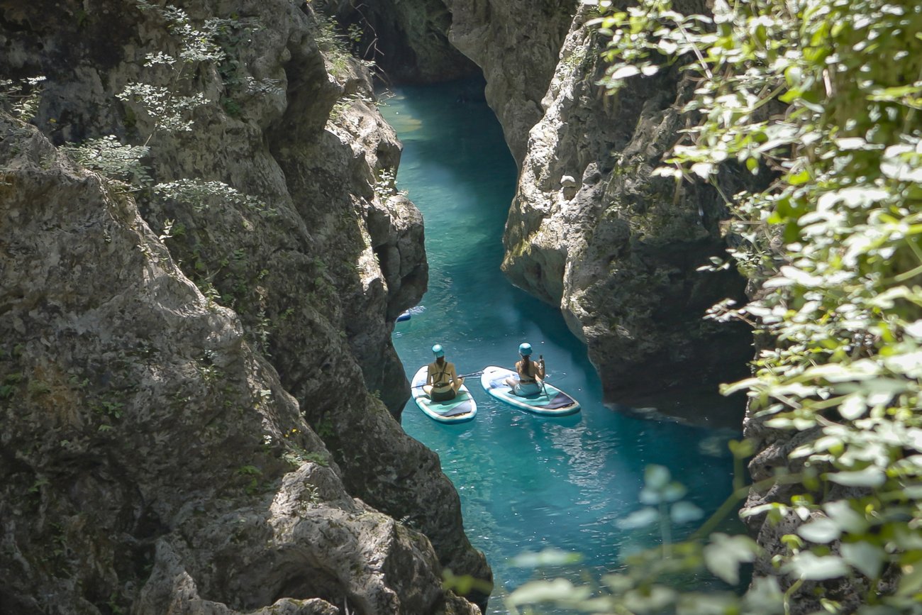 Persone in paddle board immersi nel canyon naturale del Canyon Park in Toscana, circondati da pareti rocciose e acqua cristallina